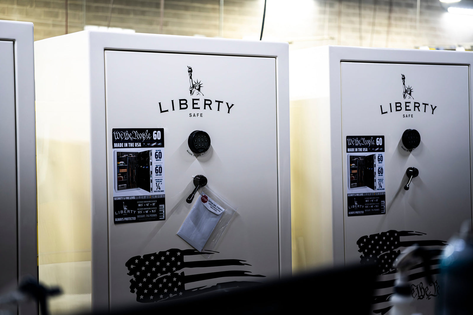 Two white Liberty gun safes with digital keypad locks displayed side by side, one featuring an American flag graphic on the door.